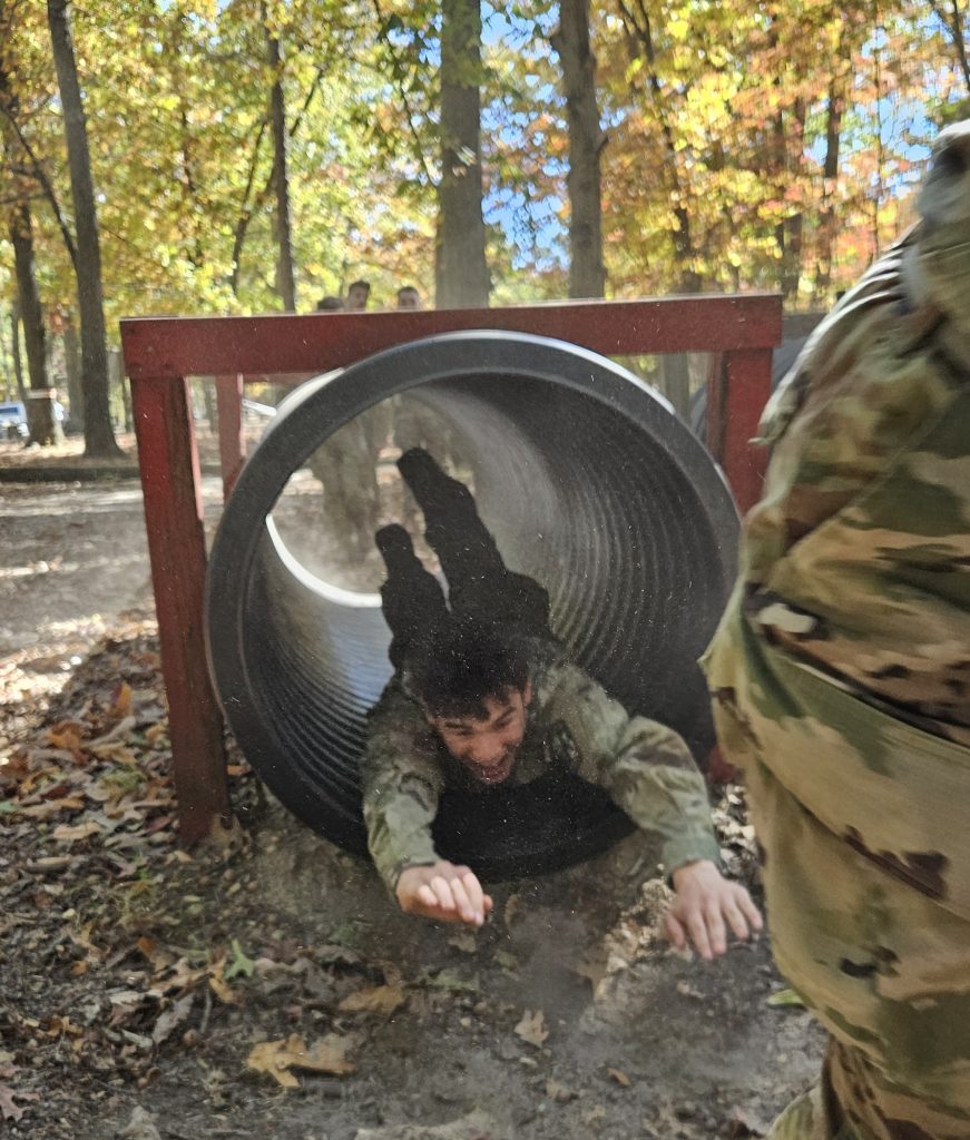 Cadet crawling through metal cylinder